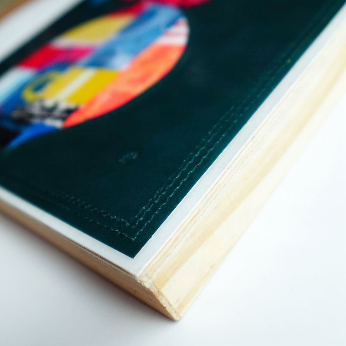 A close-up angled shot of a colorful artwork with a dark background. The light natural wood edges are visible on a clean white background.