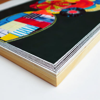 A close-up of a black machine stitching along edge of natural wood artwork panel.