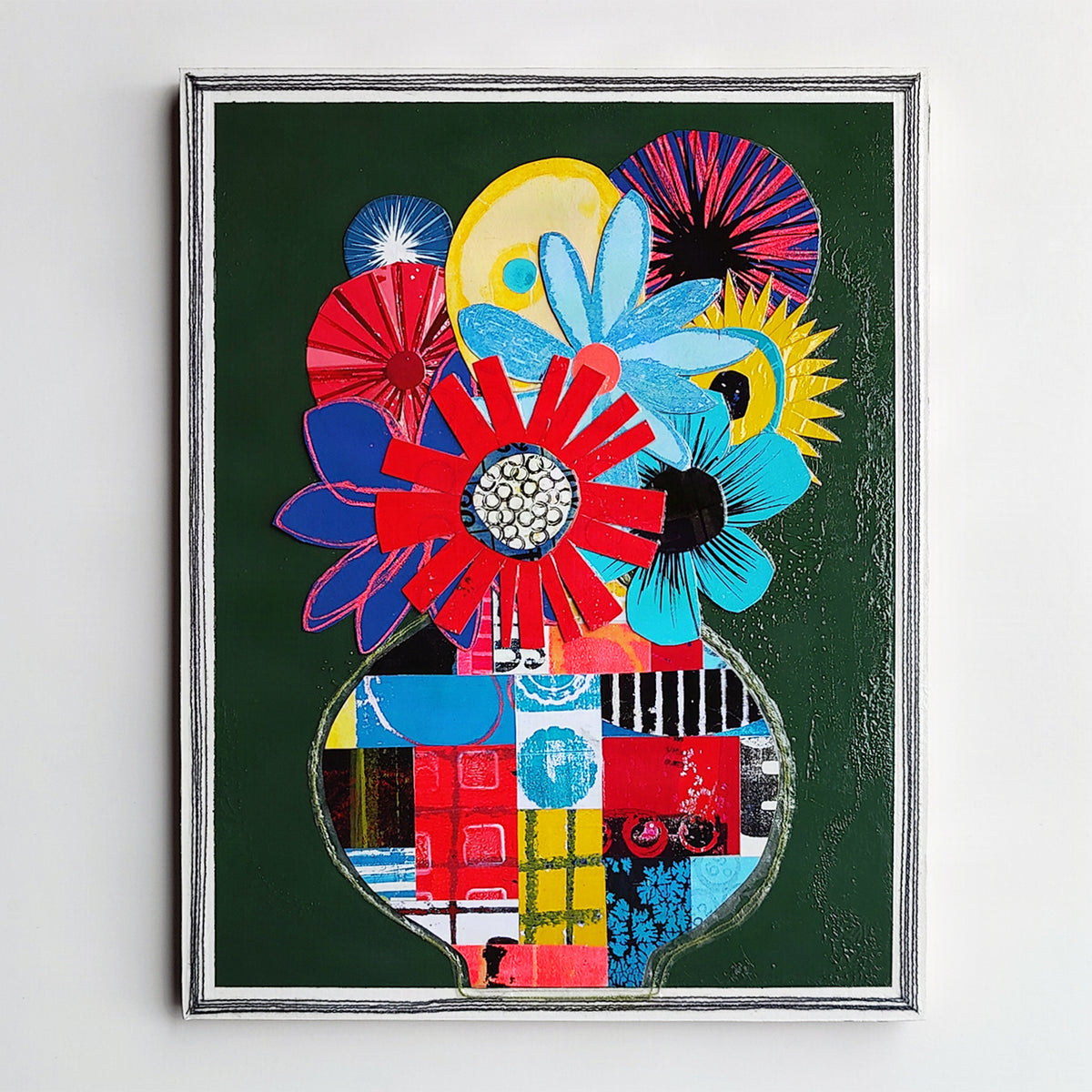 A framed abstract floral painting featuring bold red, blue, yellow, and purple flower-like shapes on a dark green background.