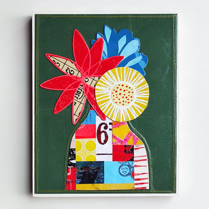 A framed abstract collage artwork on a white wall. The piece features a dark green background with layered floral and shapes in red, blue, yellow.