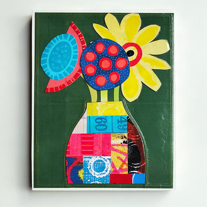 A colorful abstract floral artwork on a dark green background, featuring a yellow flower, blue and red circular motifs, and a patchwork vase in bright pink, blue, yellow, and red tones, photographed against a light neutral wall.